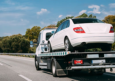 flatbed tow truck driving on the road with a white passenger car on top