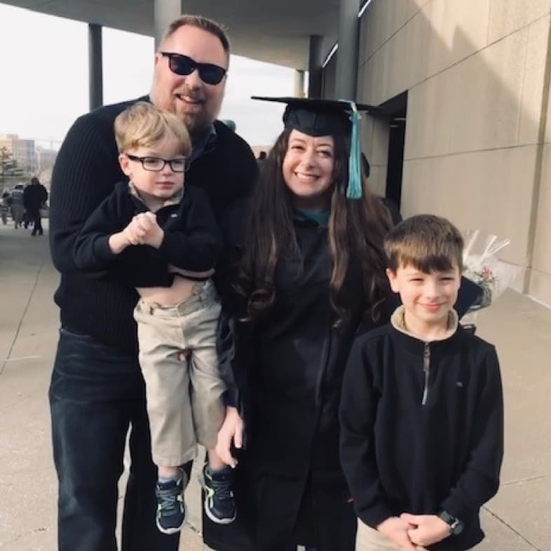 Elizabeth Lewis poses for a photo in her graduation gown with her partner and two children.