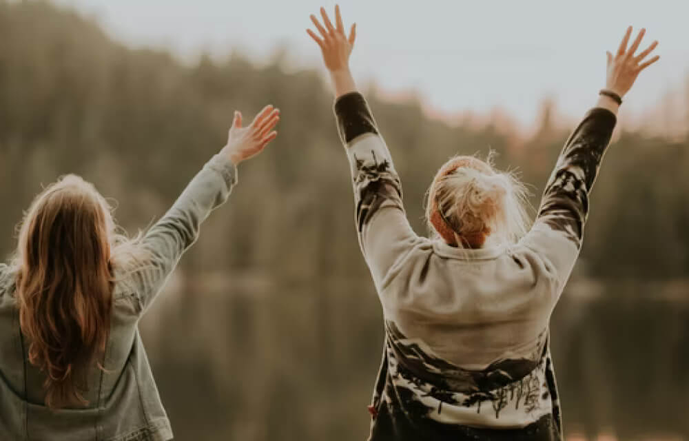 Two women in sweaters raising hands