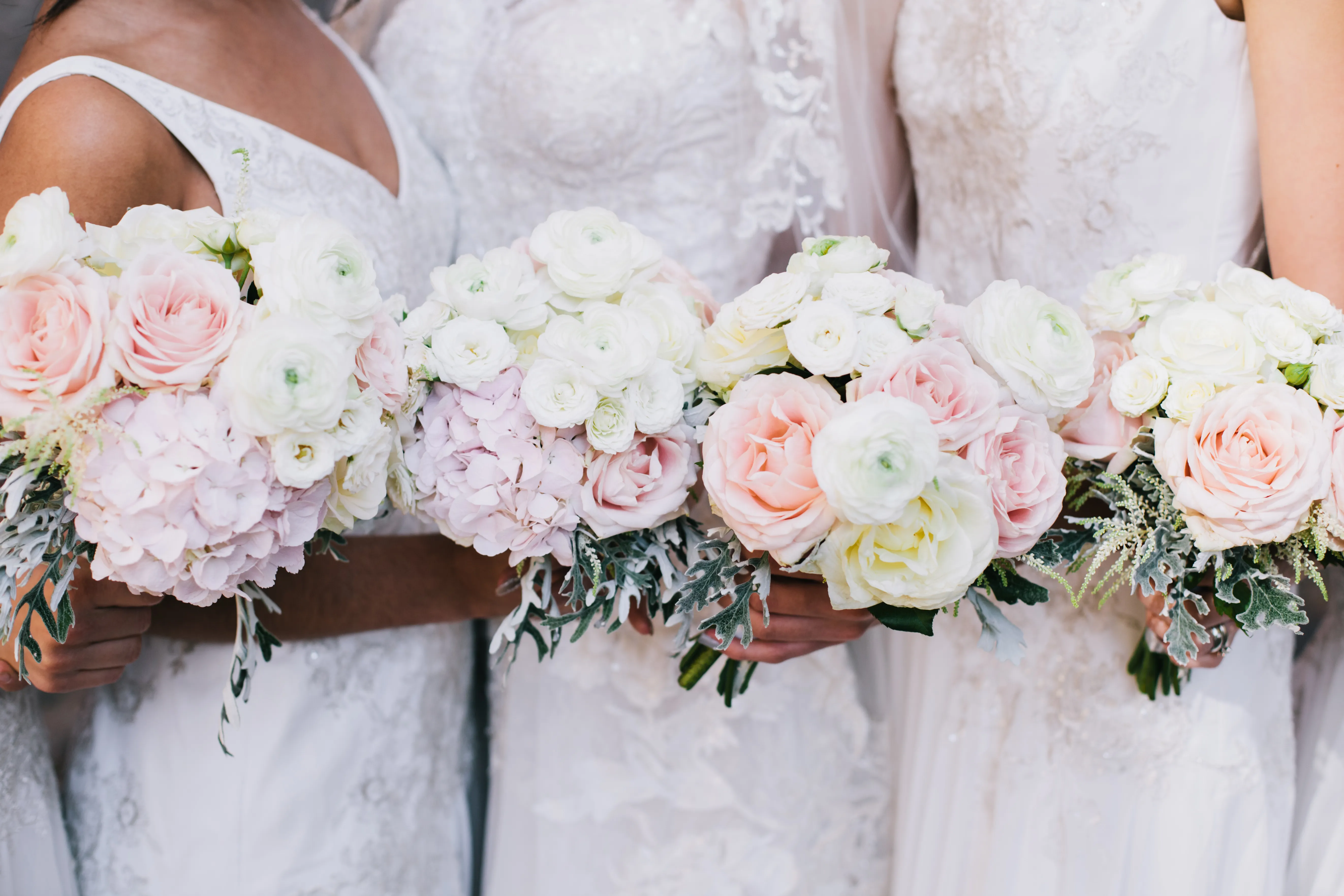 A croped image of three brides in wedding dresses, each holding a bouquet of pale pink and purple flowers