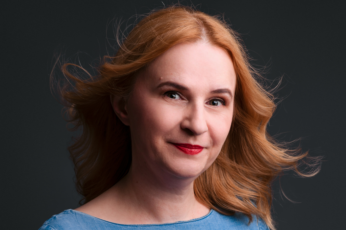 žena koja ima rak dojke u plavoj haljini lepršave kose stoji nasmijana