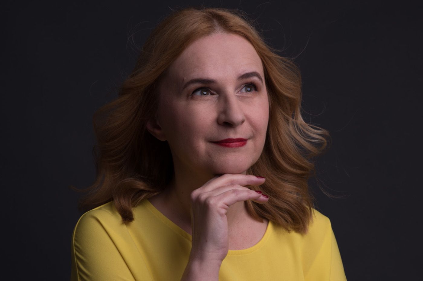 žena oboljela od raka dojke u žutoj majici lepršave kose stoji i gleda u daljinu rukom ispod brade