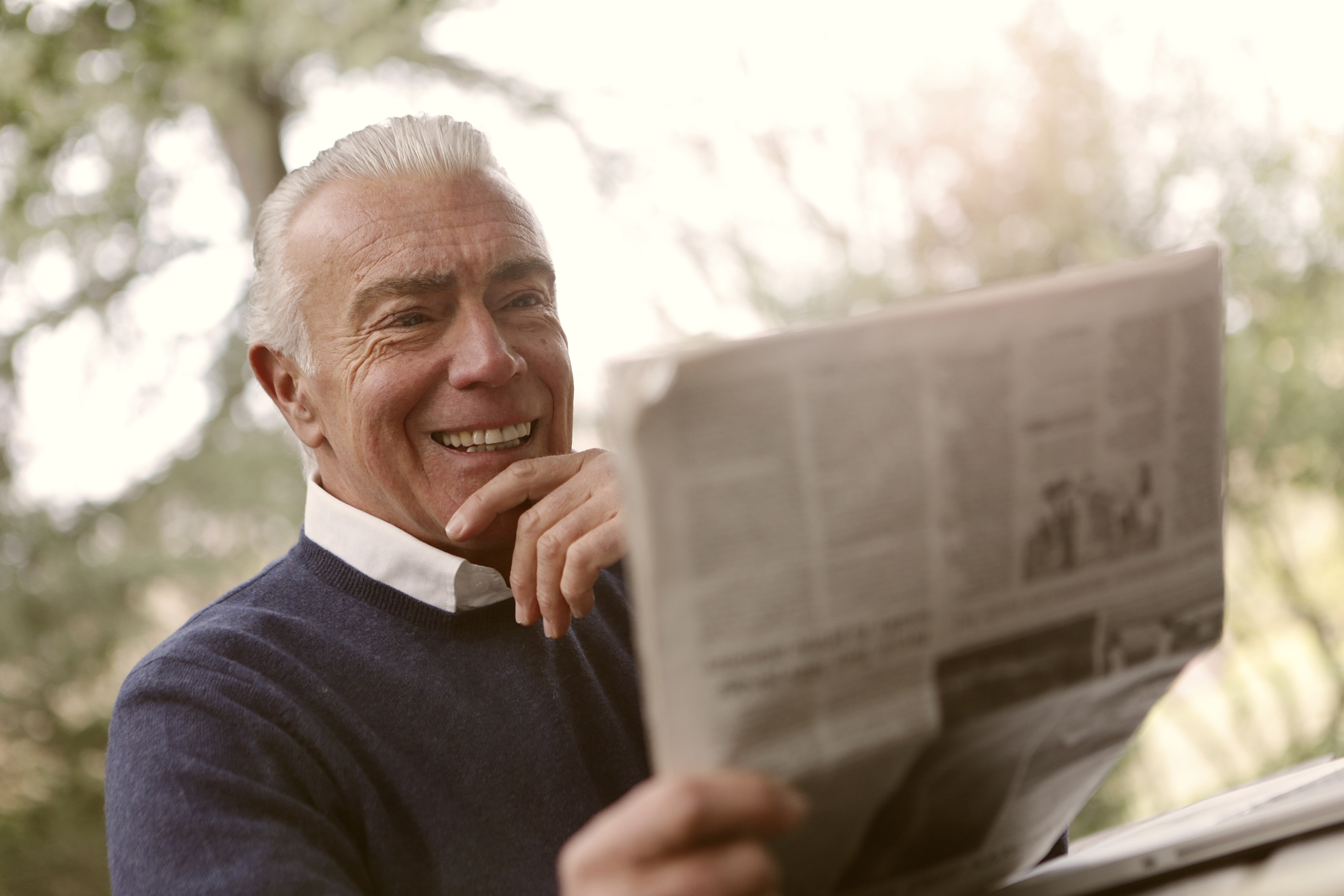 A classically handsome senior man is smiling and reading the newspaper.
