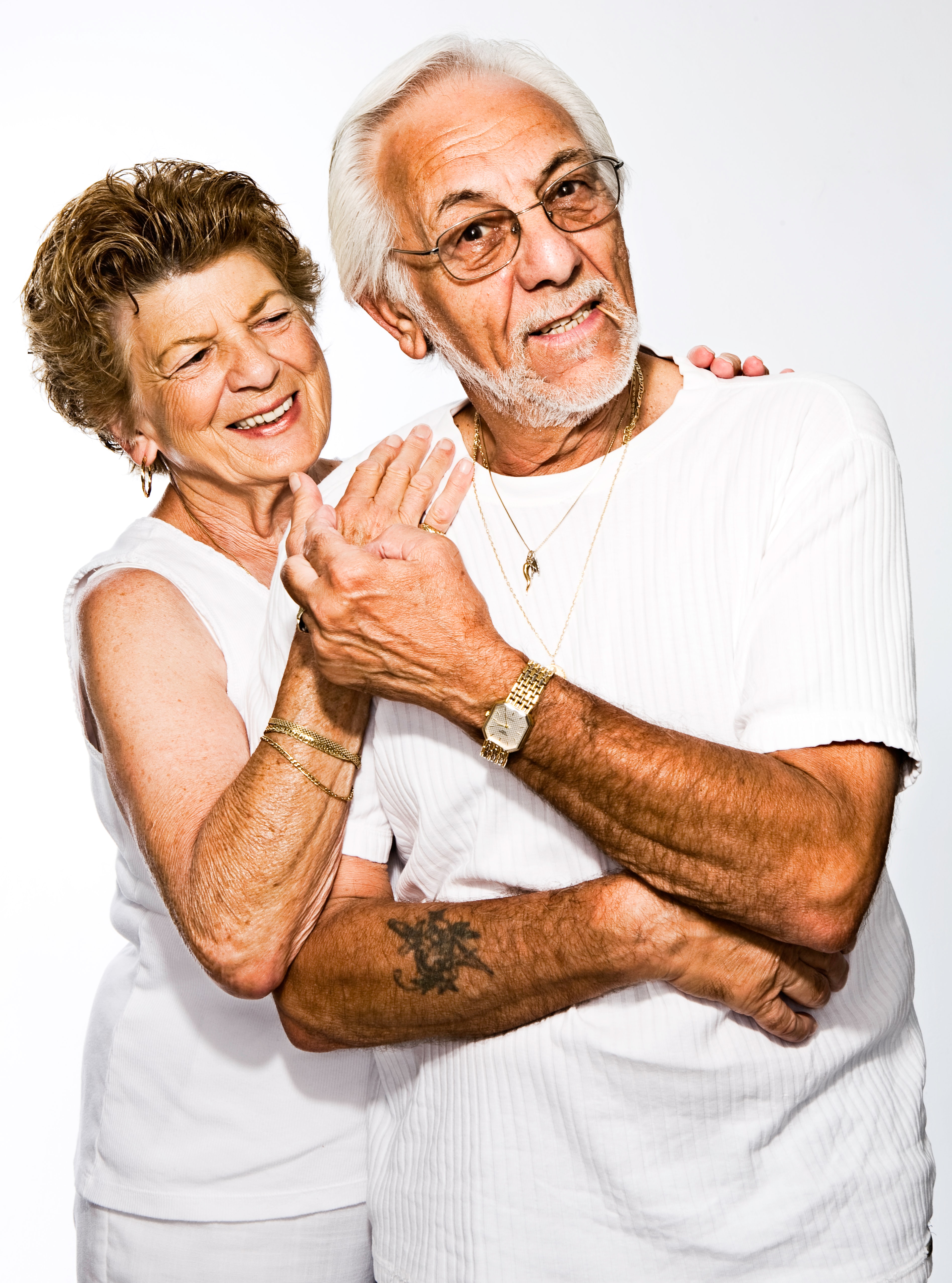 An older man and woman in all white standing together against a white background.