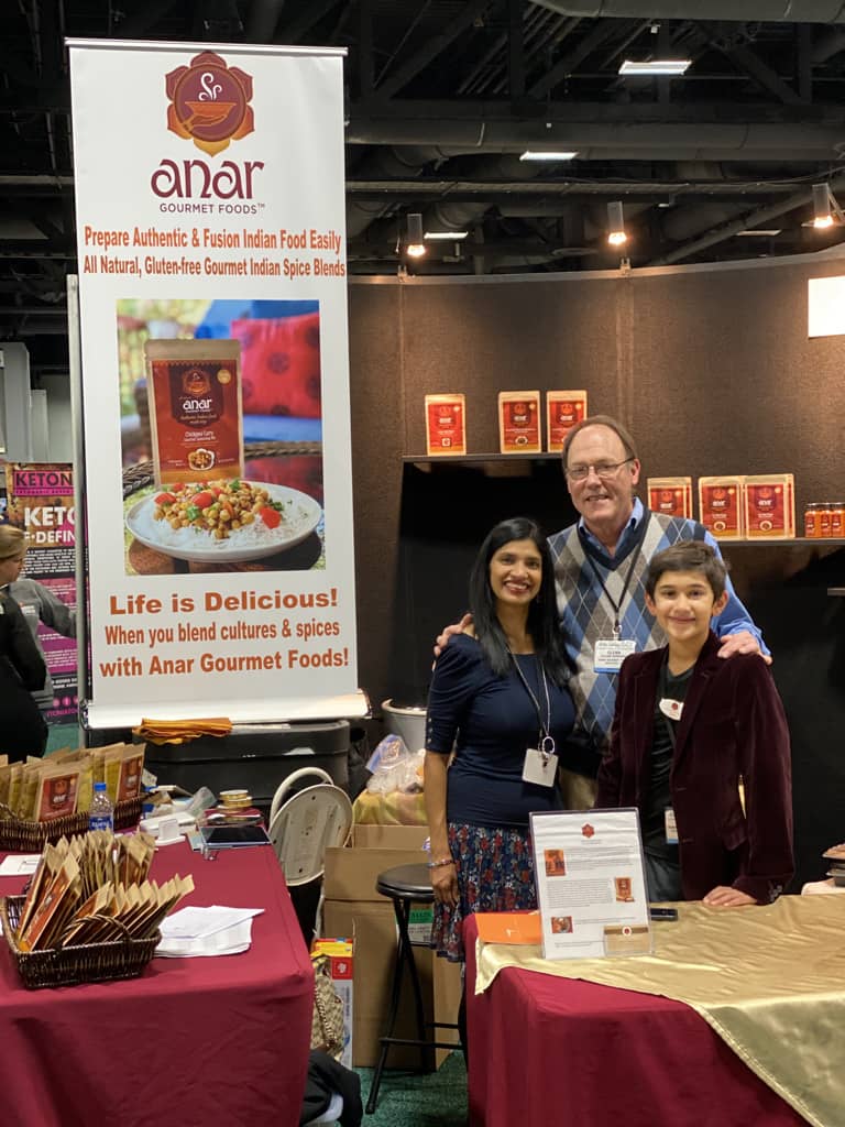 Woman, man and child standing in front of a sign with Anar Gourmet on it