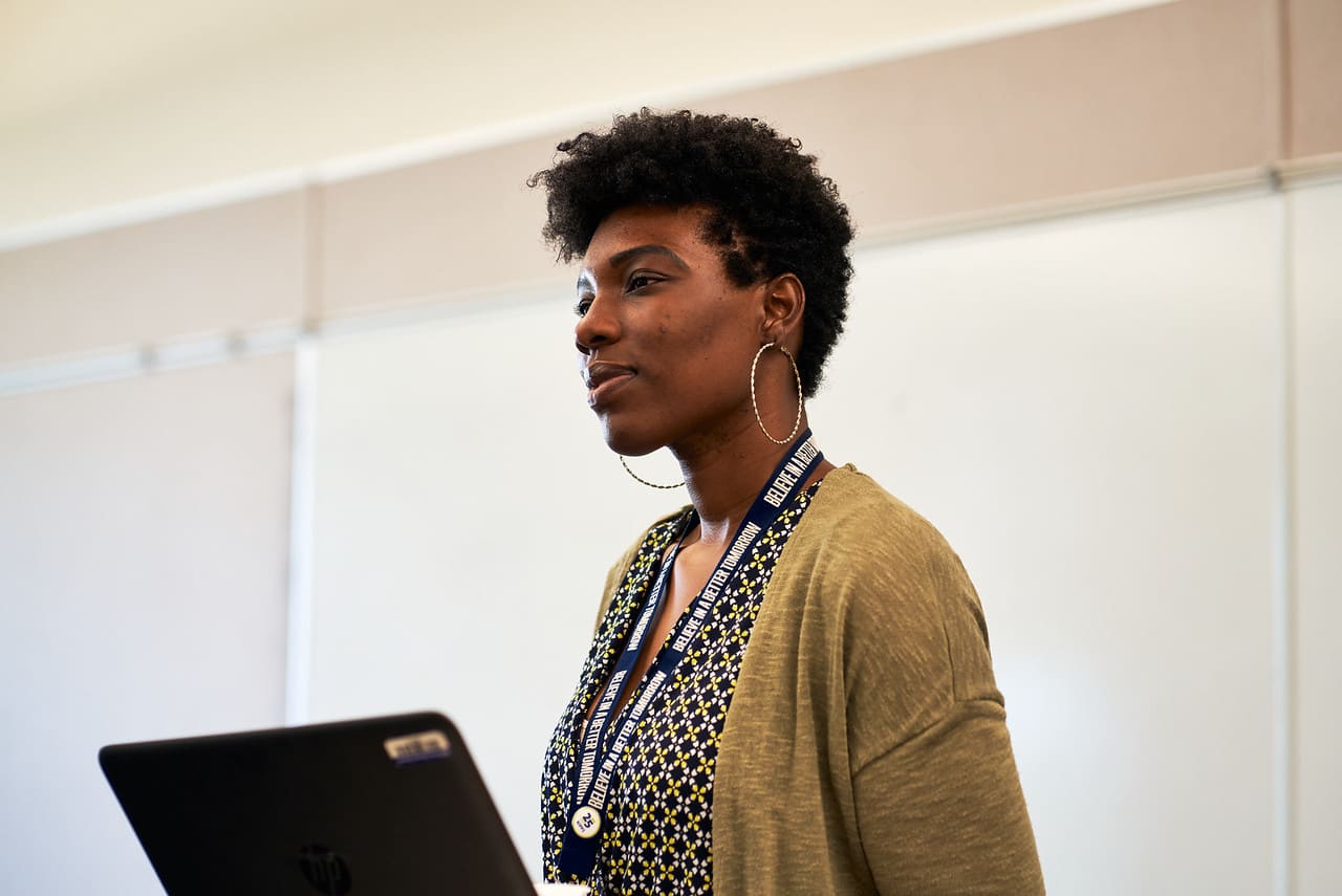 Woman speaking to fellow Relay students in front of classroom.