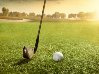 golf club setting up to hit a golf ball on artificial grass putting green