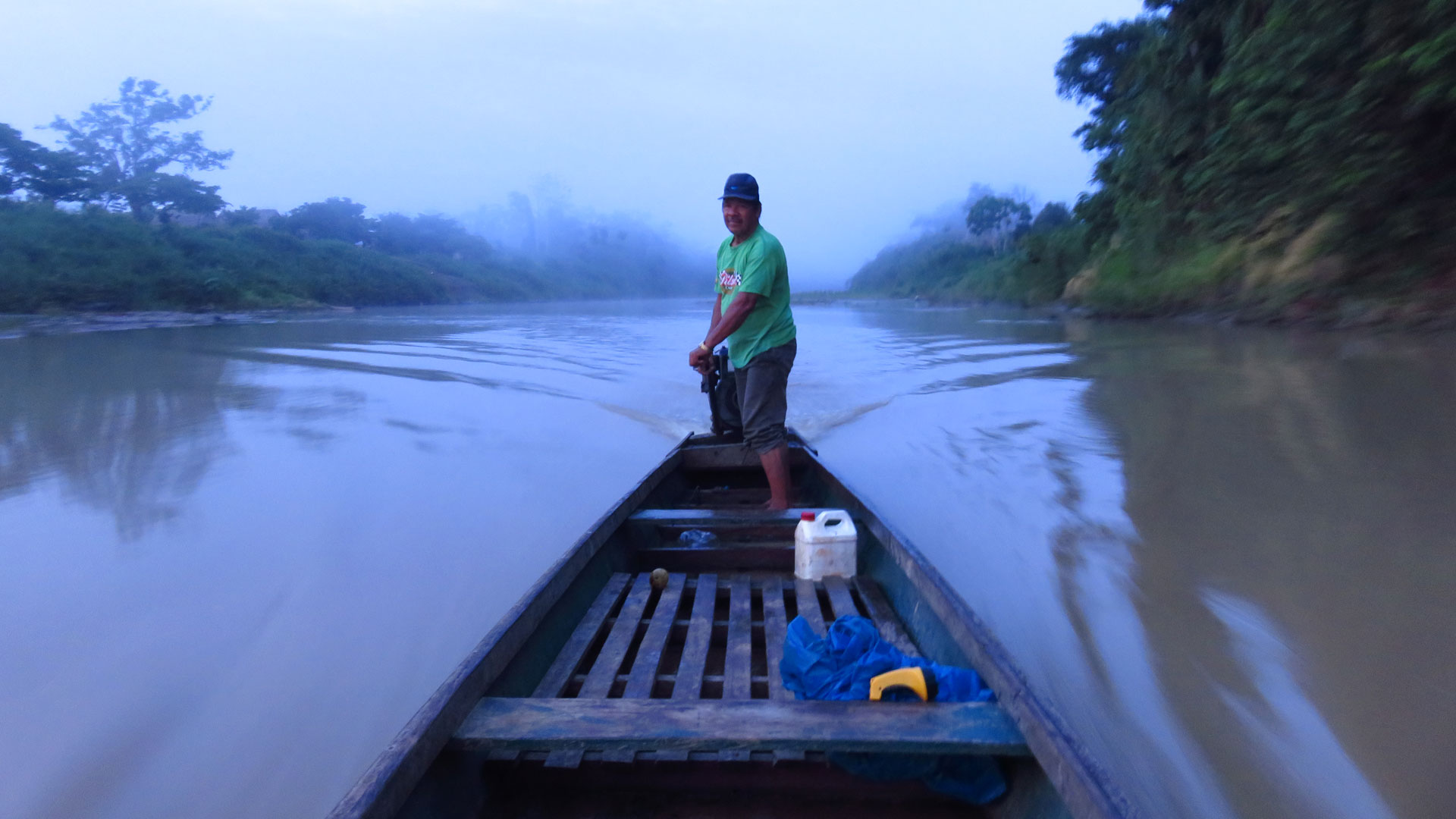 A man steering a small wooden motorboat along the river