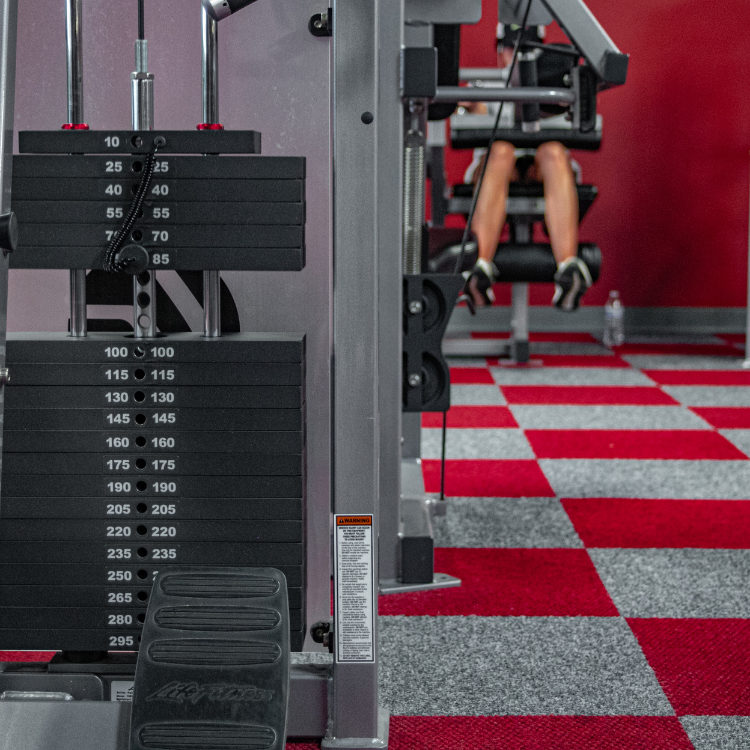 Machine weights with woman using leg lifting machine in the background