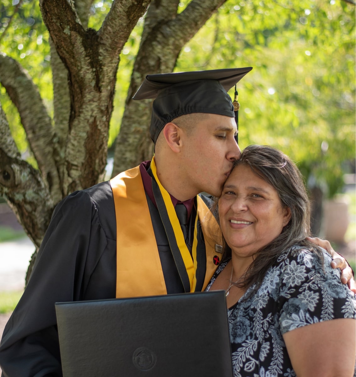 Image of a student at his graduation holding his diploma and hugging his mother