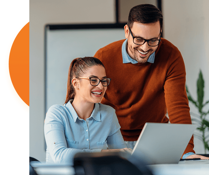 Man and woman with glasses smiling at a laptop.