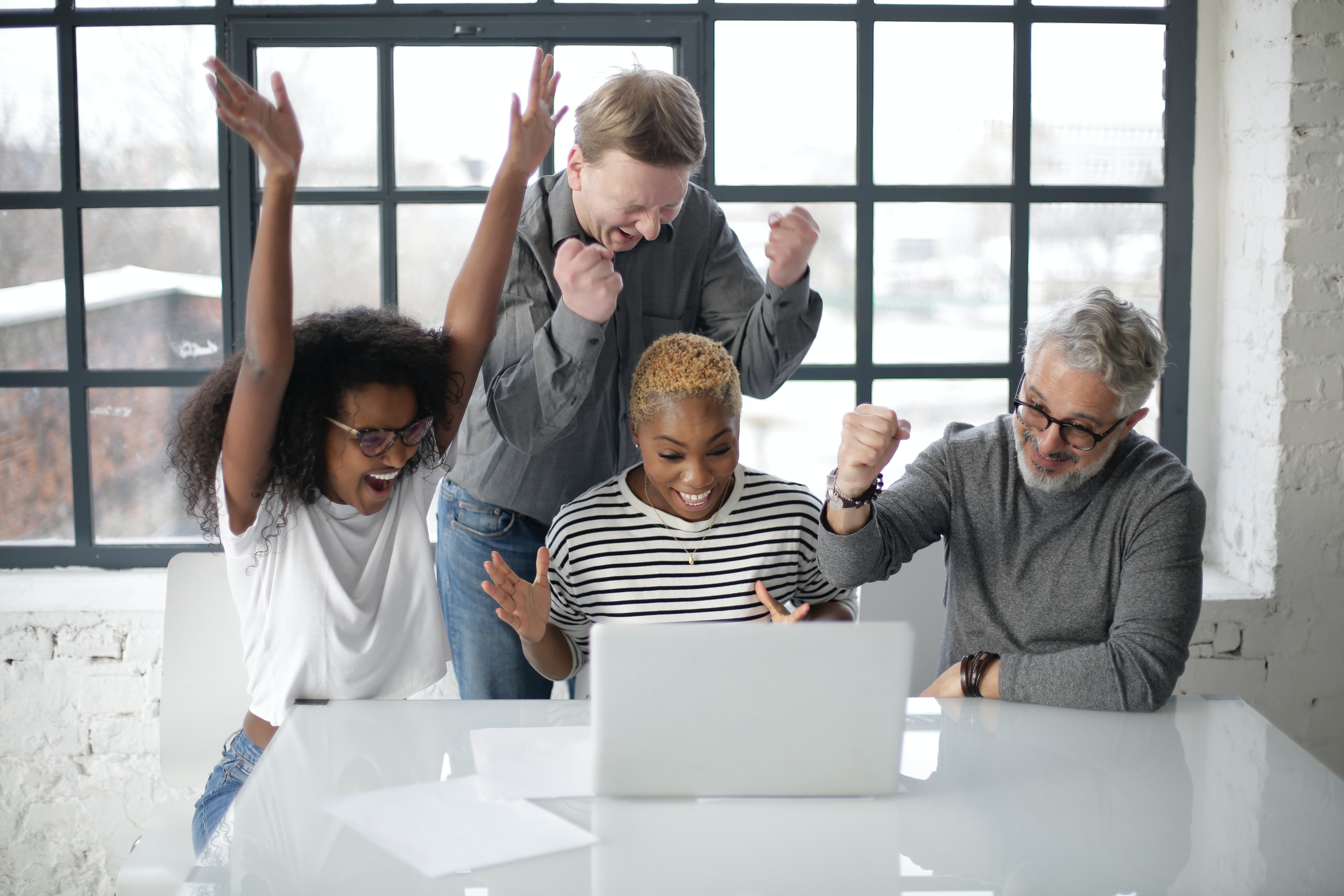 Excited multiracial colleagues enjoying triumph together in front of laptop in office