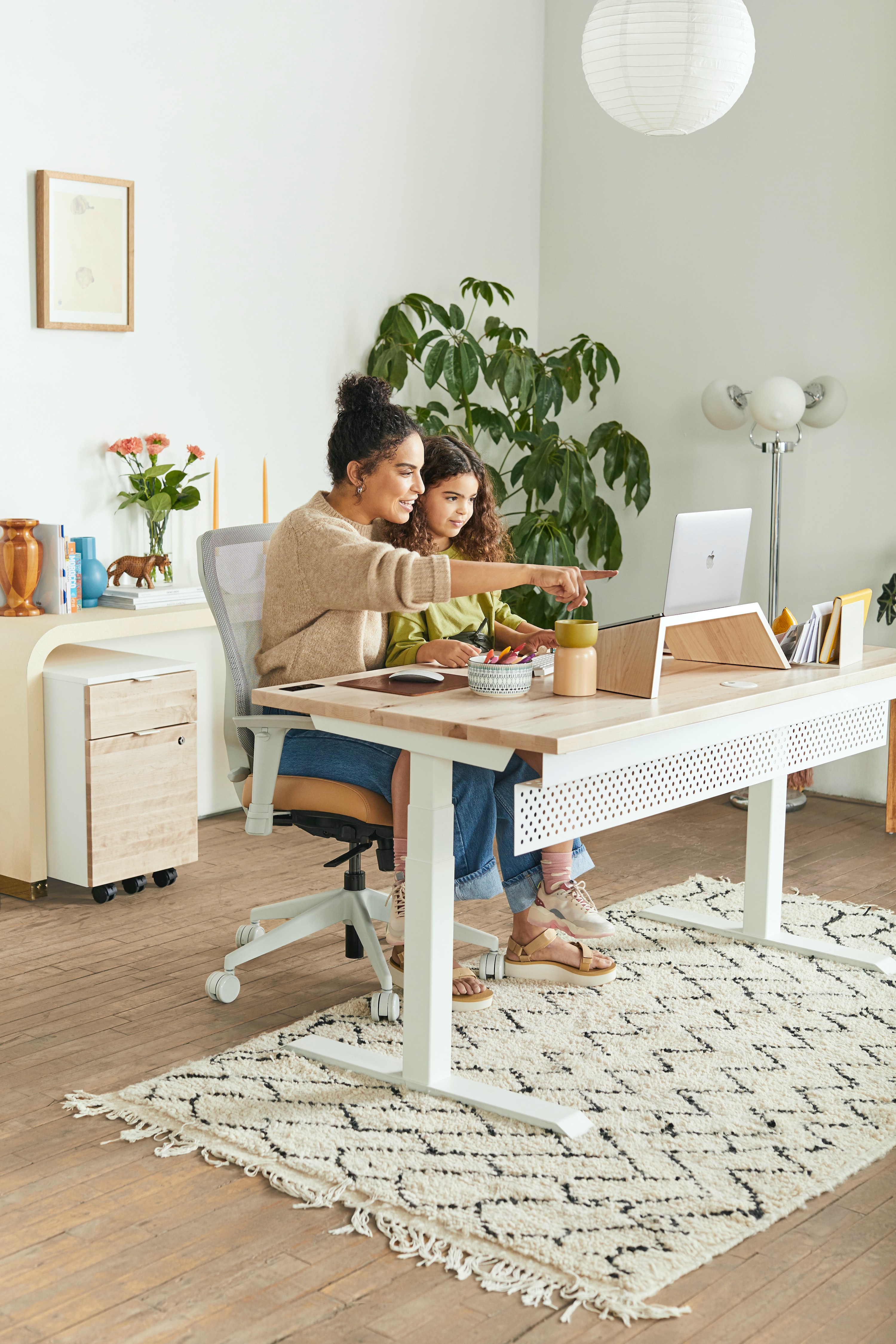 Mother and young daughter in a minimal-style office space looking at a screen together. The mother is pointing at the screen.