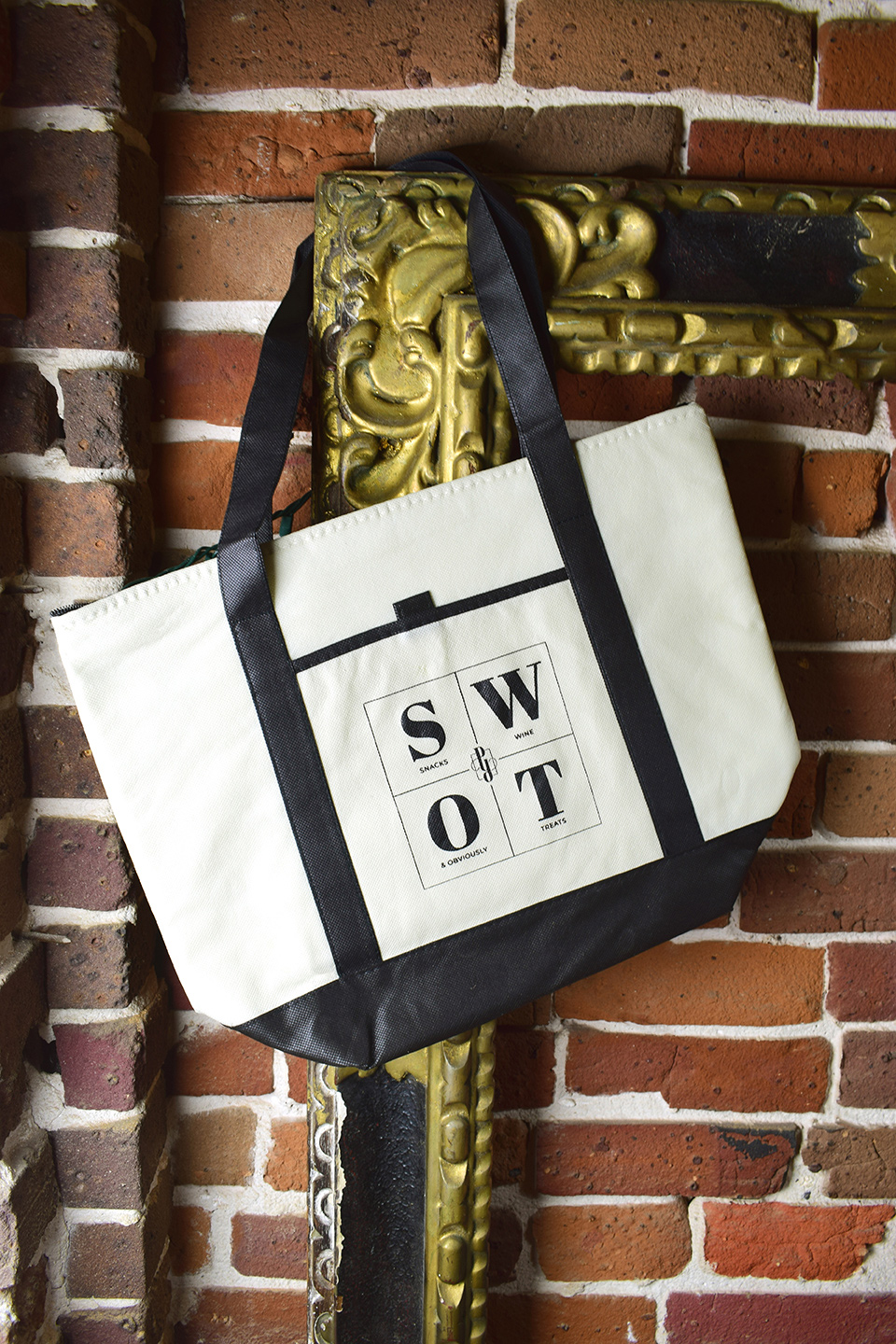 A photo of the branded "SWOT" bag hanging off a gold frame