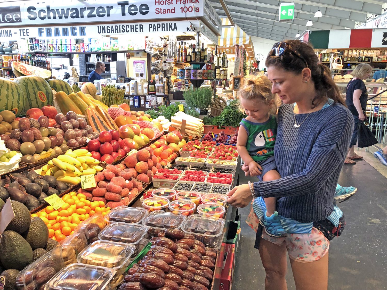 Blog author Corrie in a market looking at produce with her child.