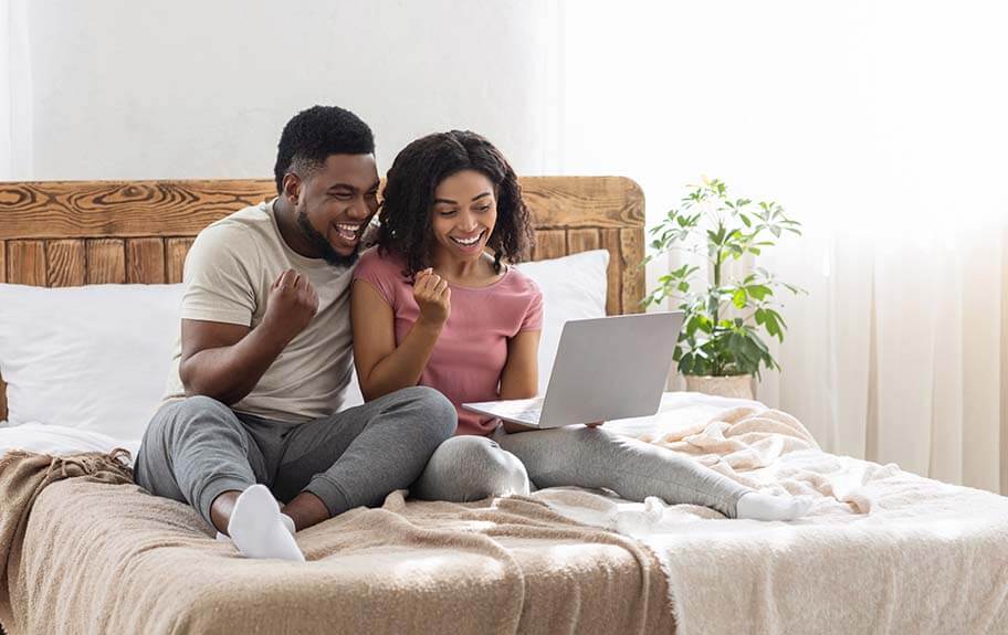 Two people sitting on a bed with a computer