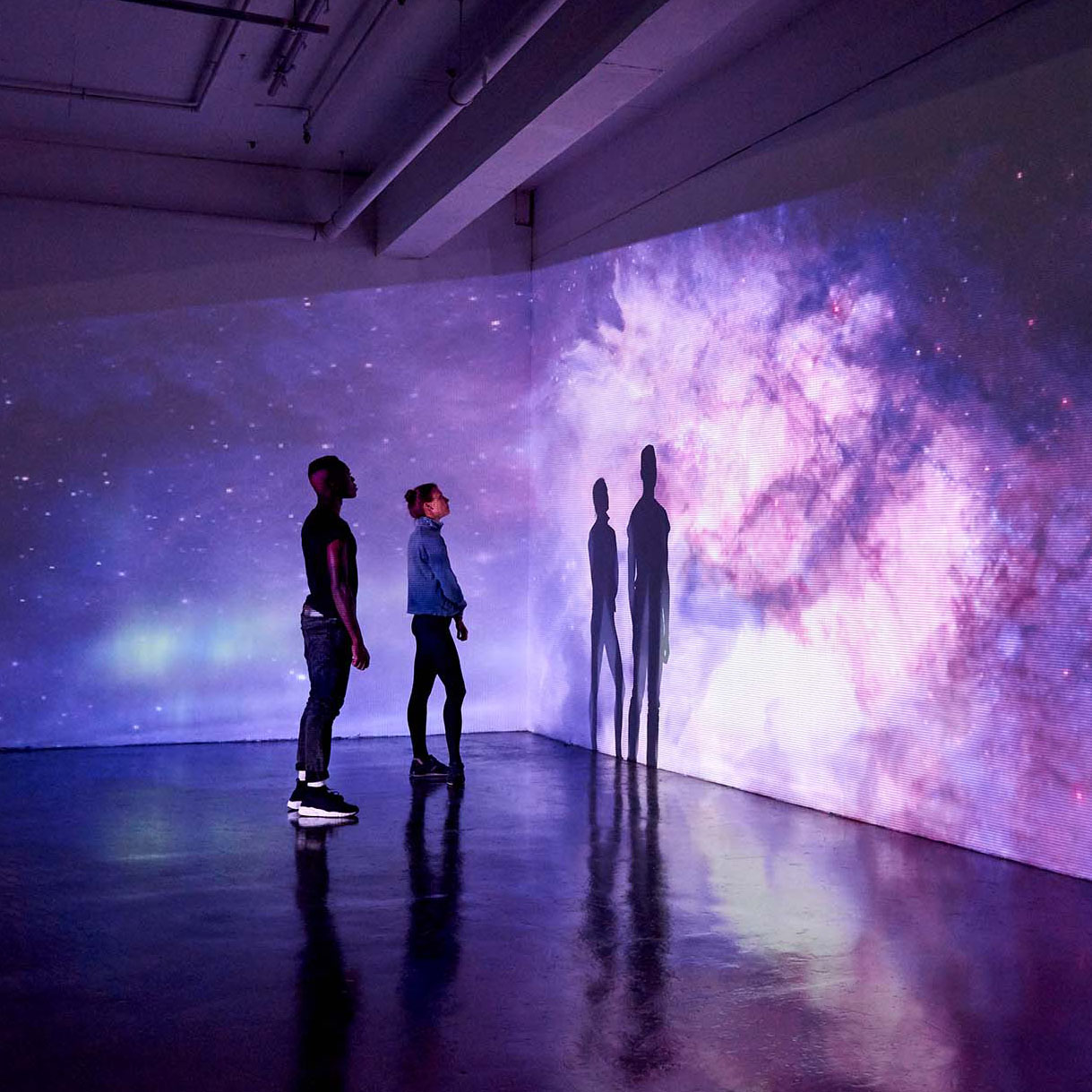 Two young adults looking at a wall that has a projected image of a galaxy on it