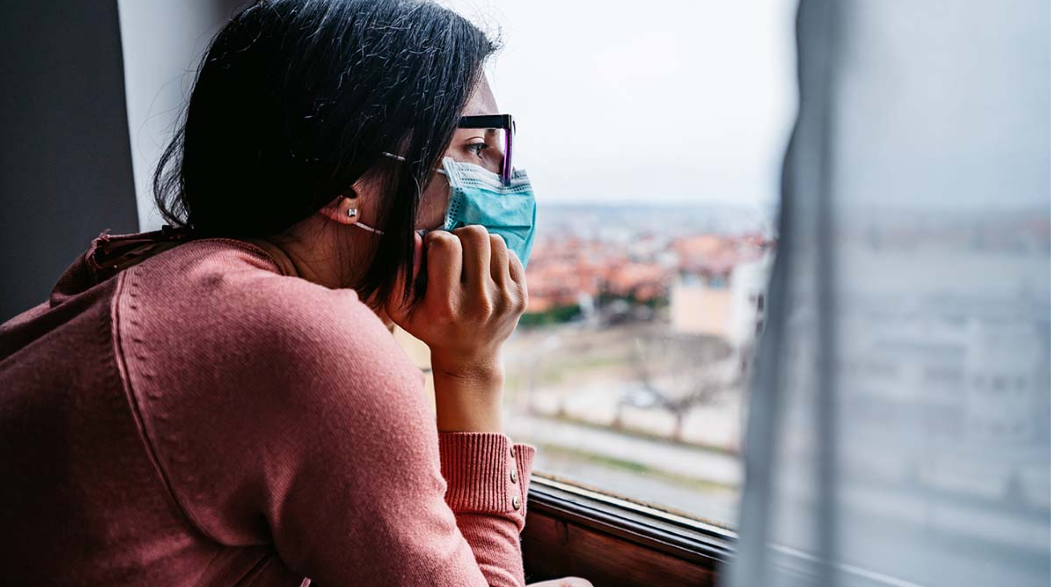 Woman wearing a mask, watching through a window.