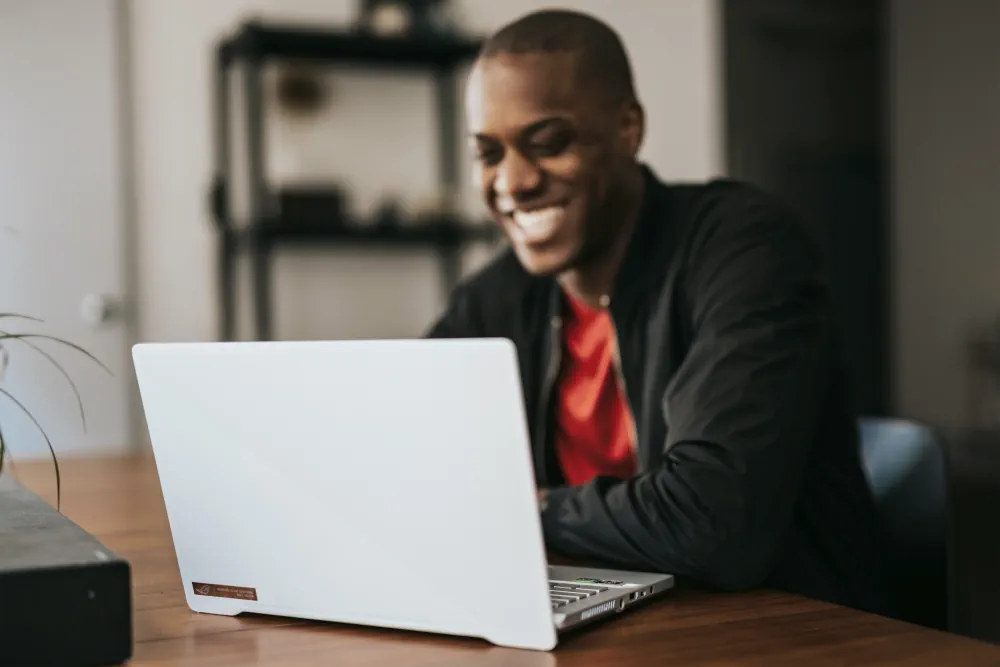 A man smiling and watching a Derek Prince sermon on a laptop