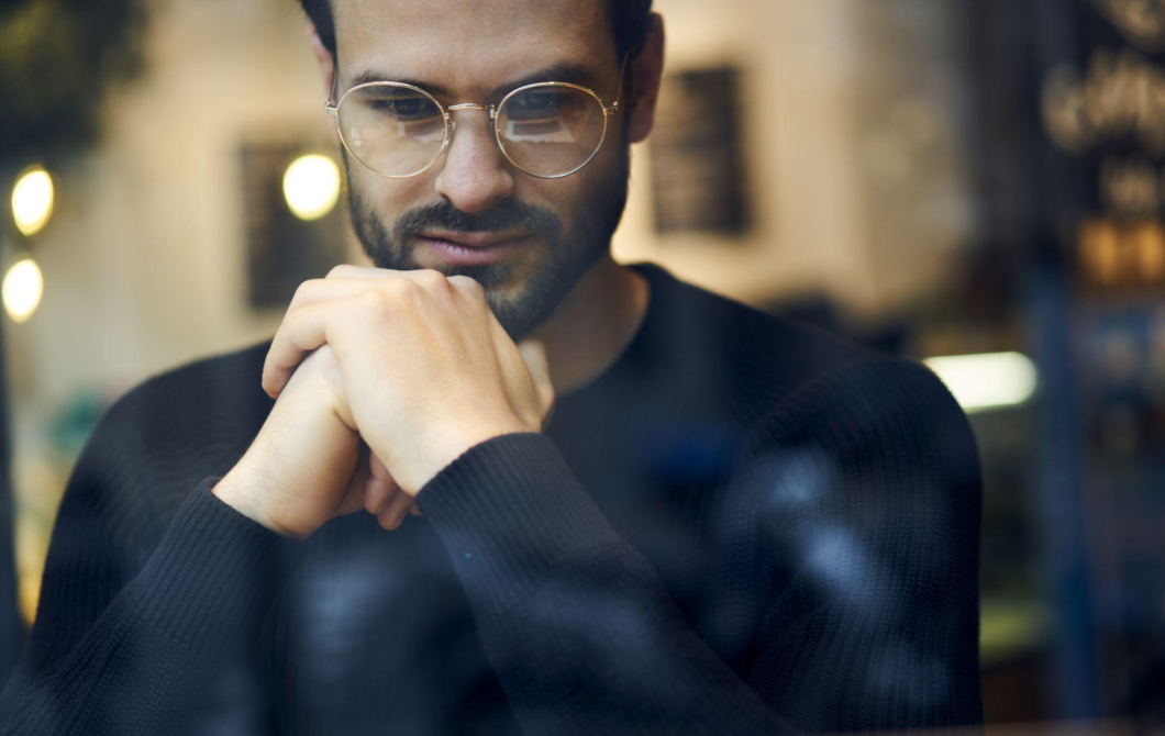 A man in glasses looks down, puzzling over the difference between sadness and depression