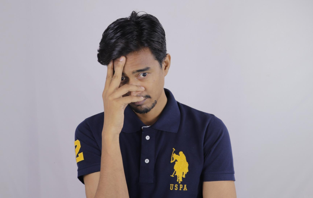 An anxious man covers his face with his hand, wondering if he needs therapy