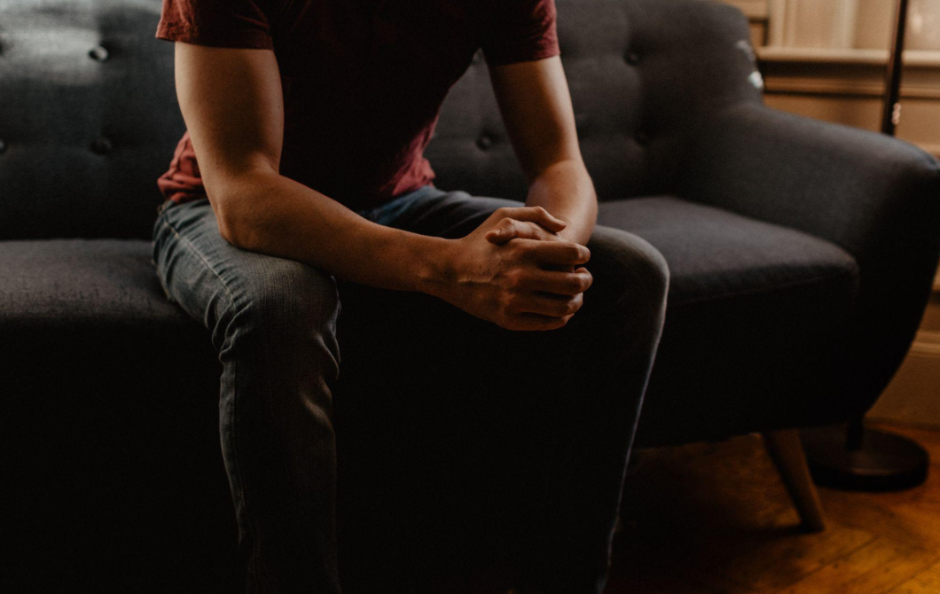 A man's body on a psychoanalyst's sofa, his hands clasped as he describes his upbringing