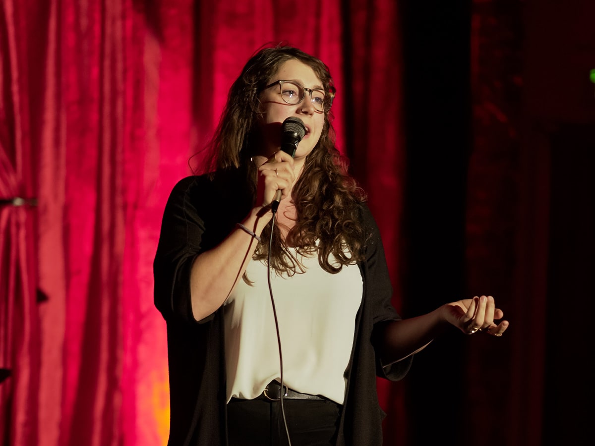 Erin Ingle on stage with a microphone doing standup