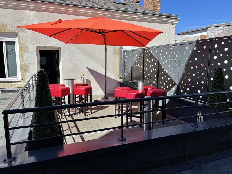 Terrasse ensoleillée avec parasol rouge et tabouret haut