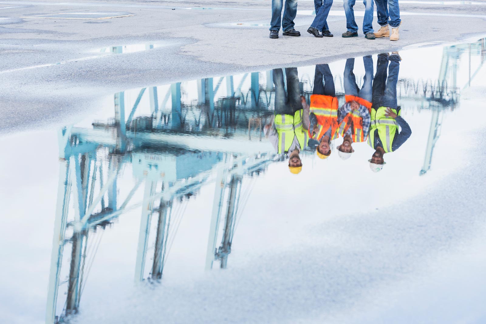 Reflection of water in parking lot of people working with reflective jackets and hardhats