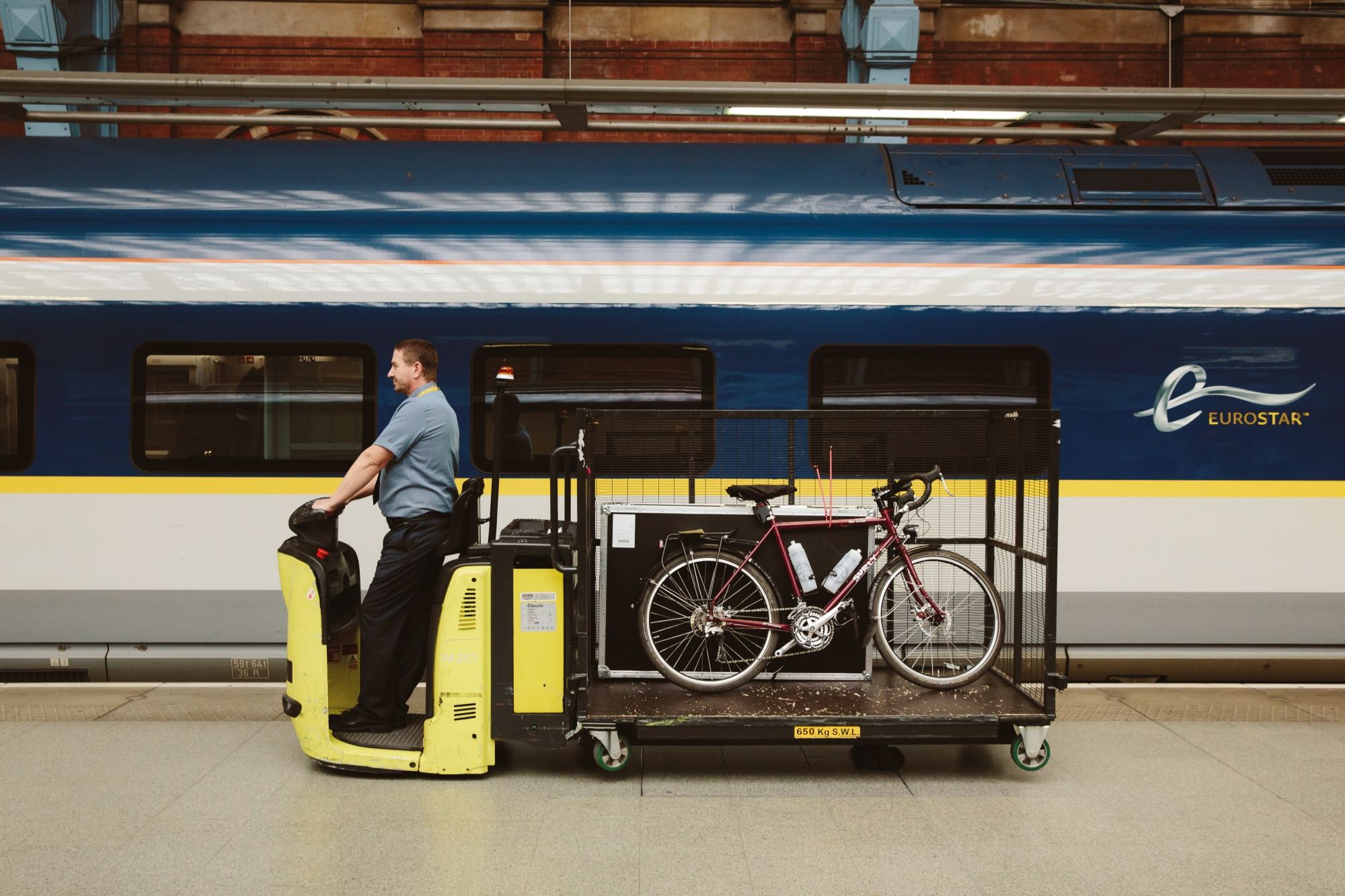 A luggage car on a station platform carrying a bike in front of a Eurostar train
