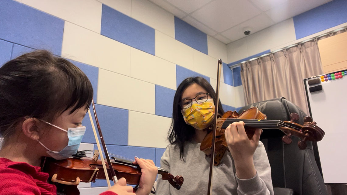 Jamie teaches a young girl how to play the violin