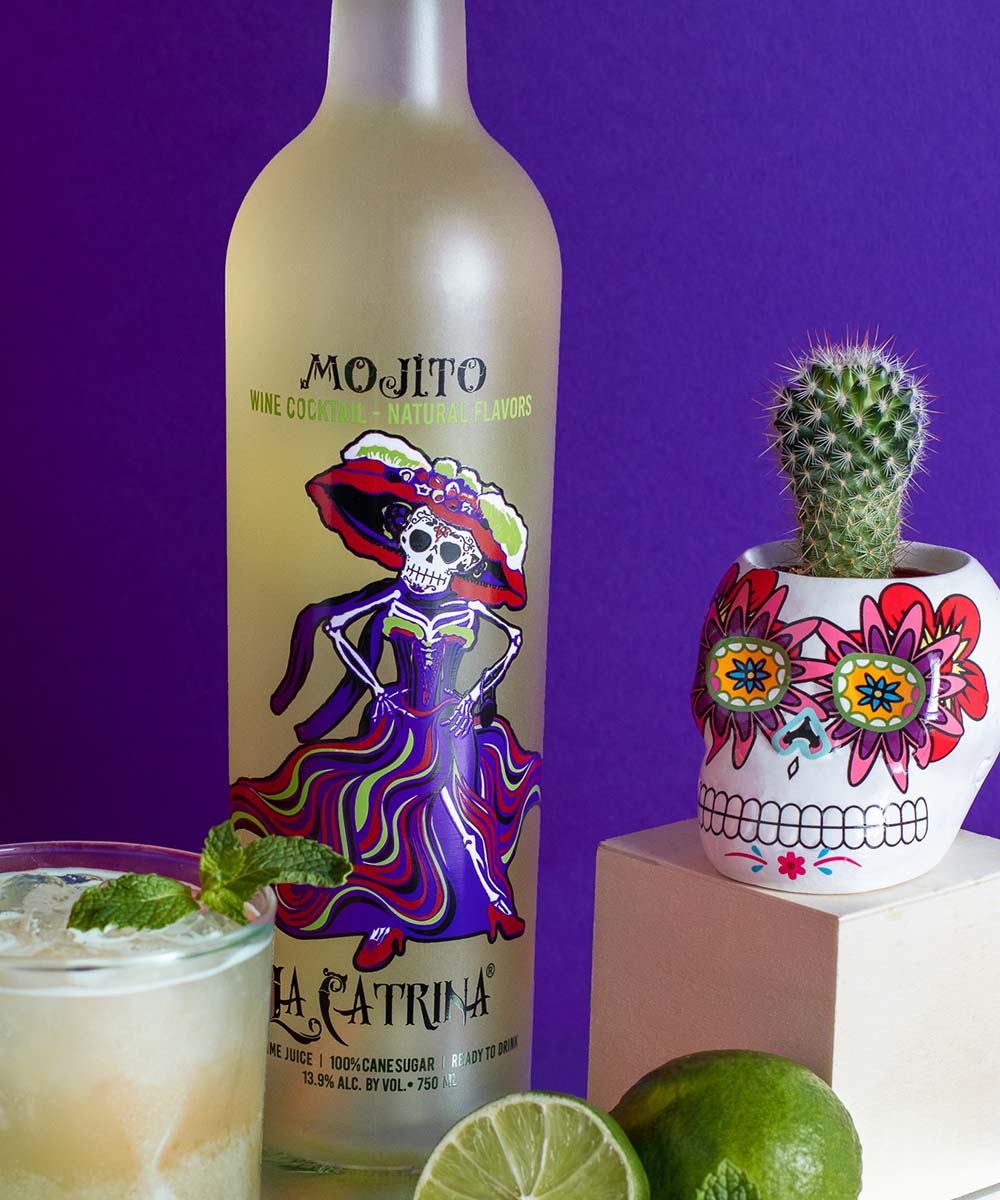 La Catrina Mojito Cocktail bottle next to a mojito glass, Day of the Dead skull and a cut lime