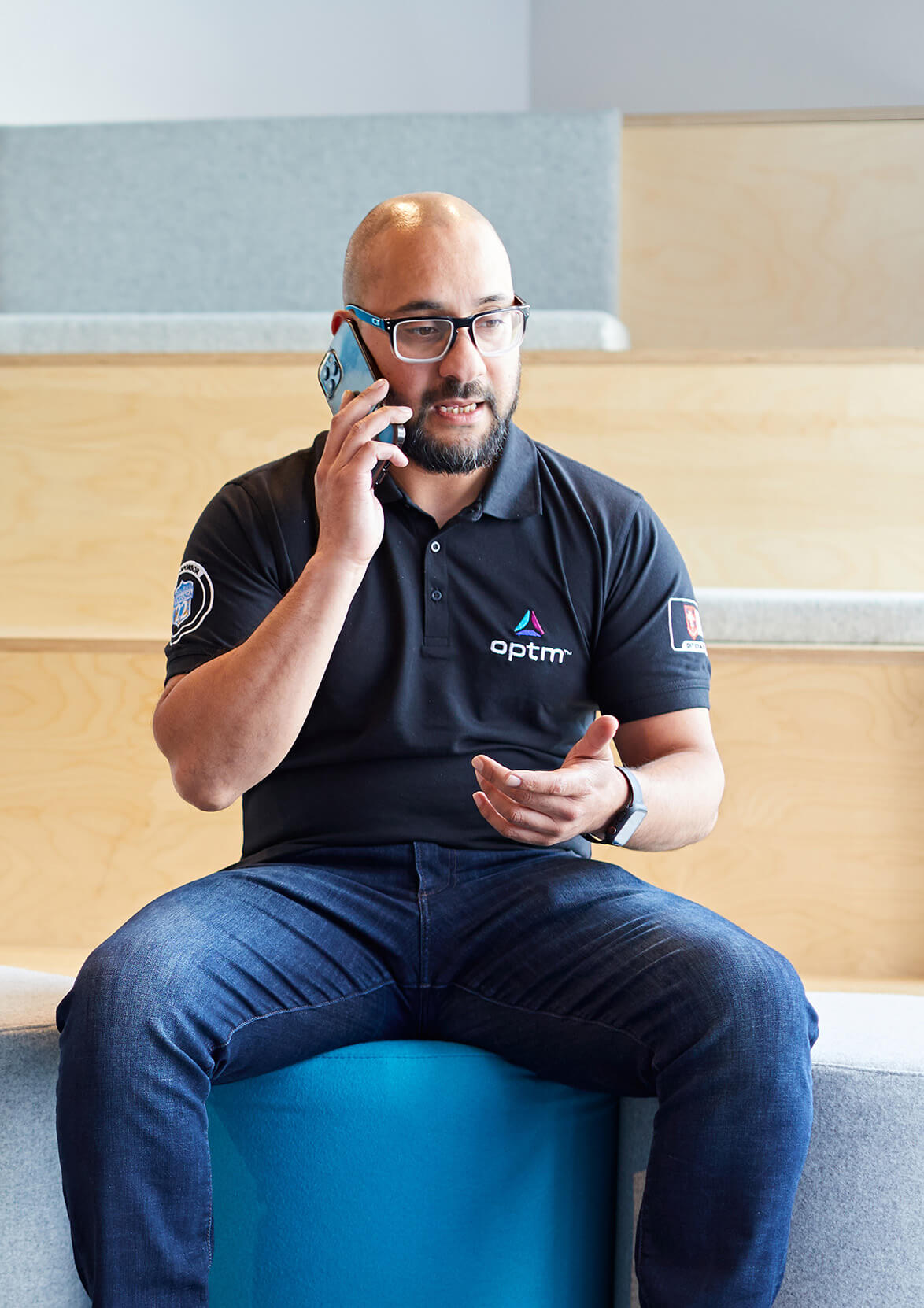 Man on phone sitting down wearing Optm polo shirt
