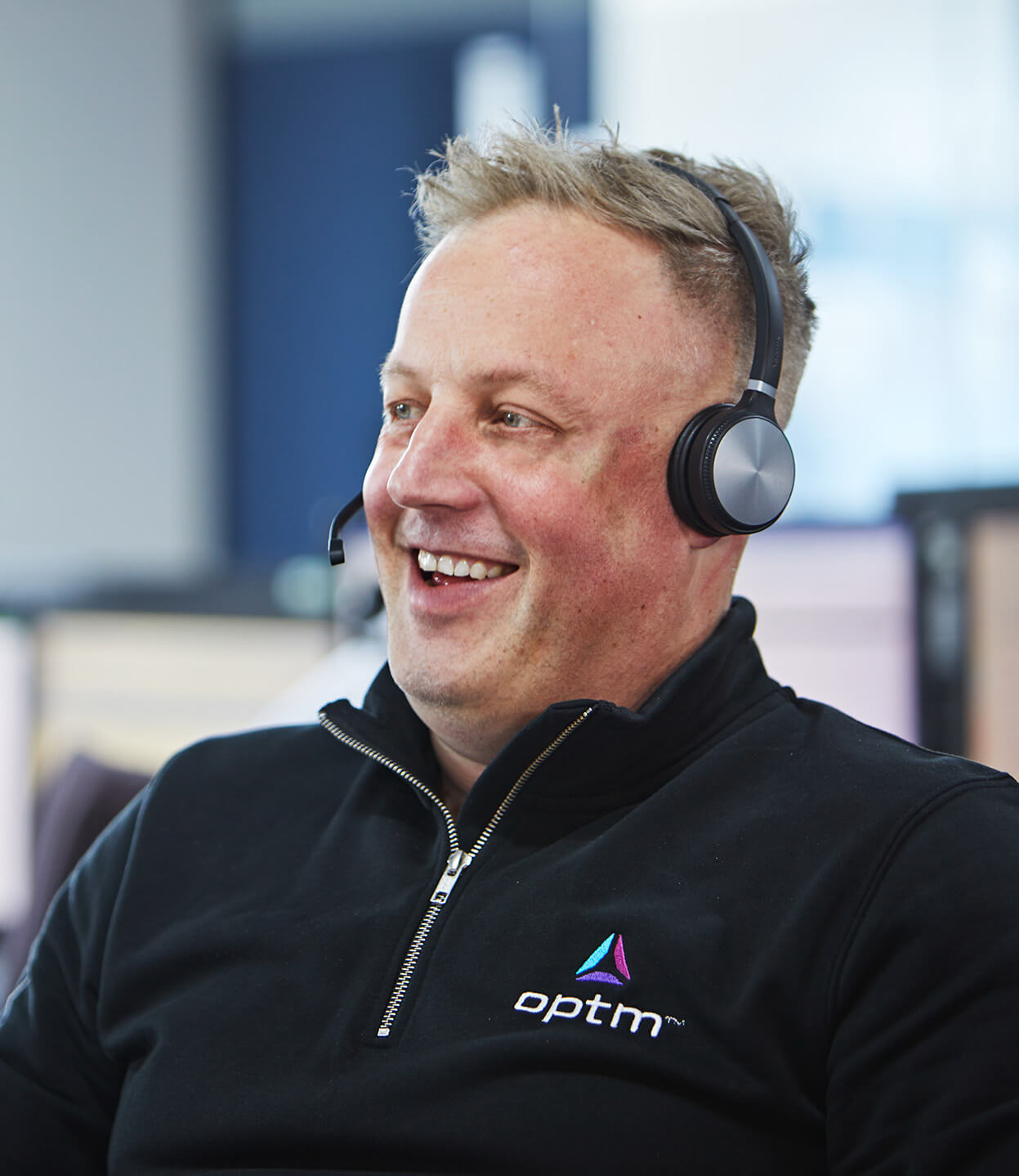Man wearing headset and Optm jumper smiling