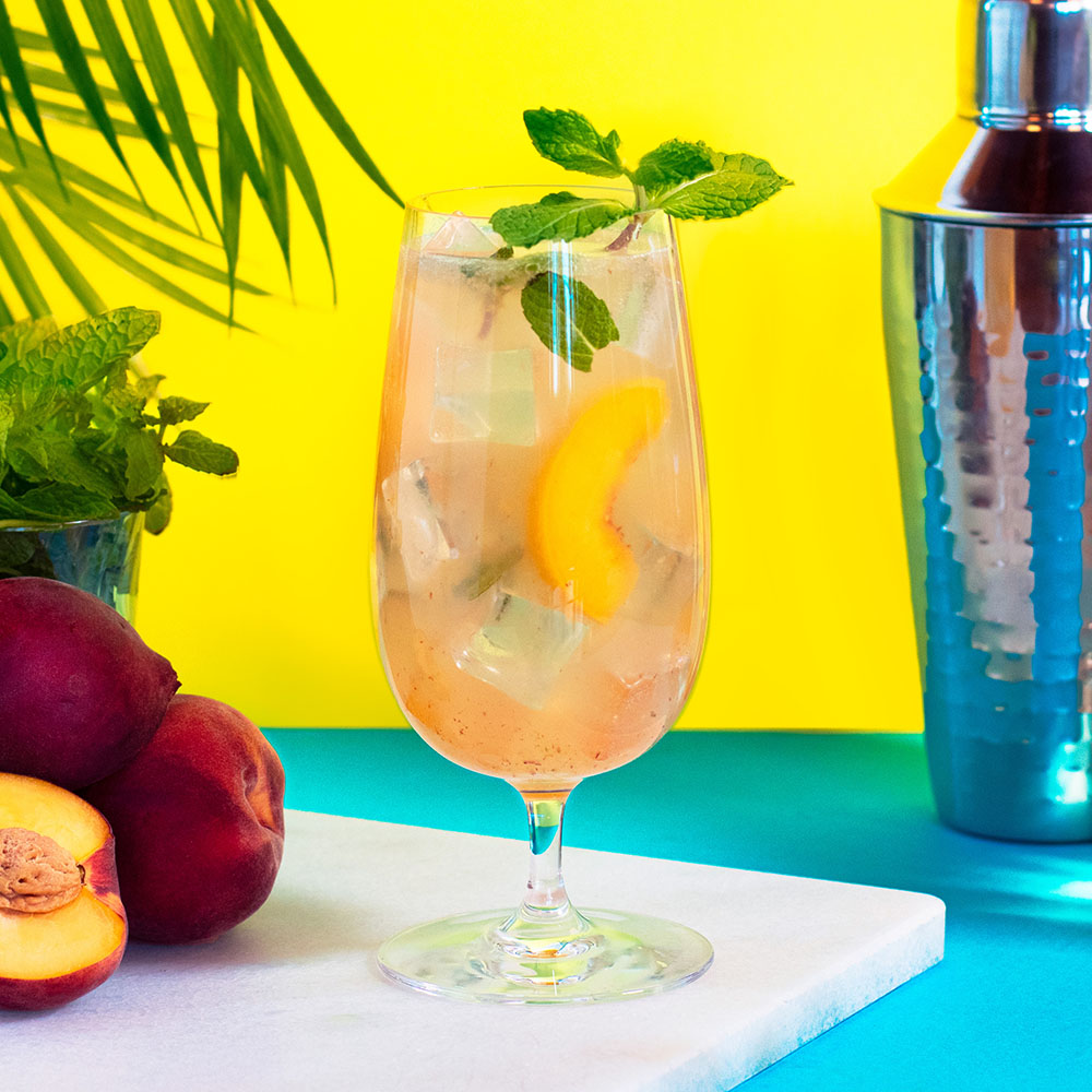 A "Just Peachy" cocktail on a table with a fresh sliced peach.