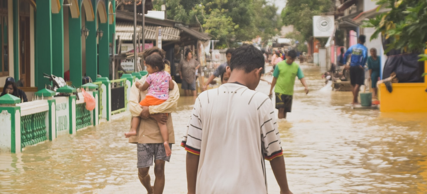 Image of a young boy standing in dirty water that is filling up the street