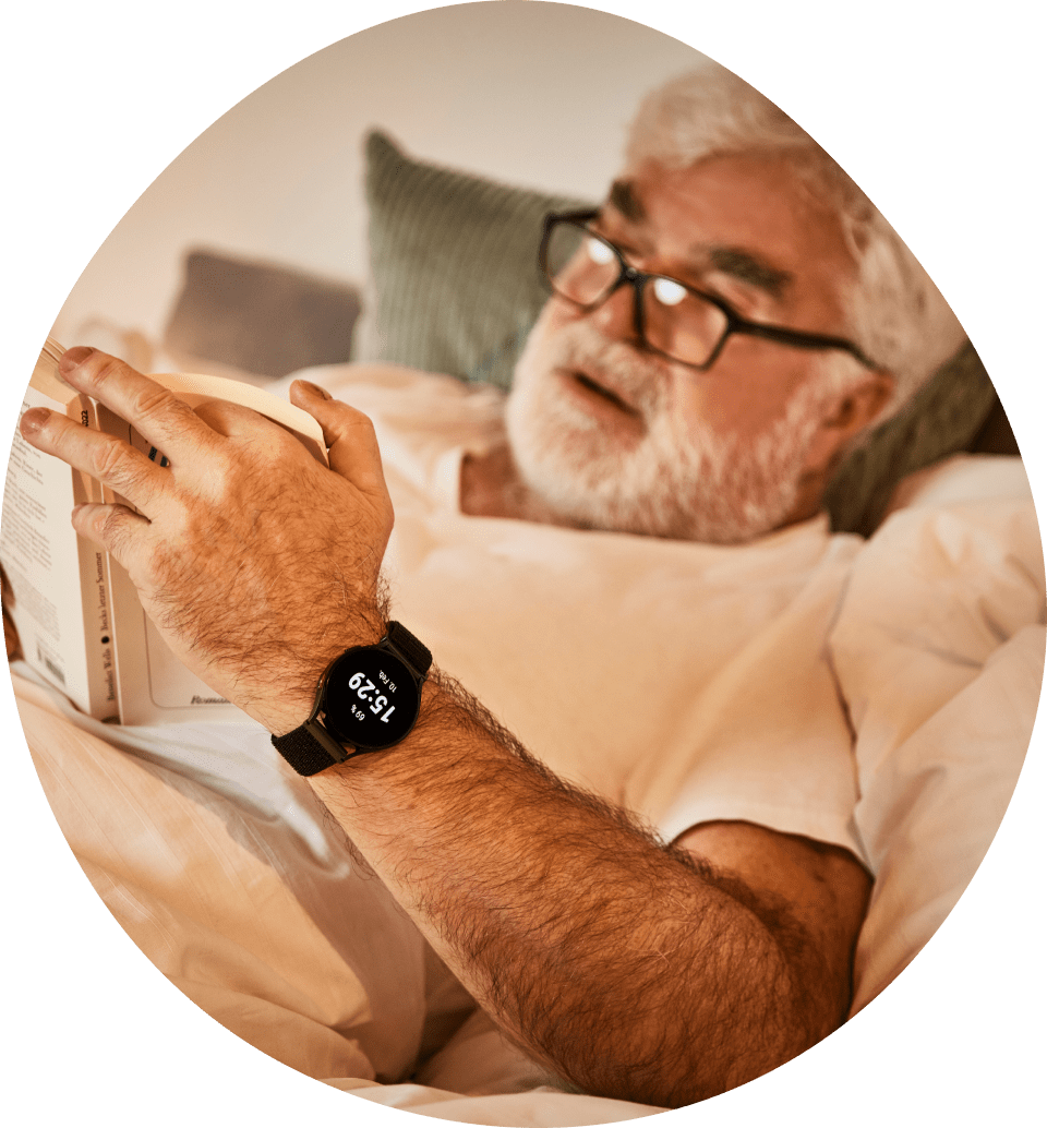 Senior mit Notfall-Uhr von Patronus liest ein Buch im Bett