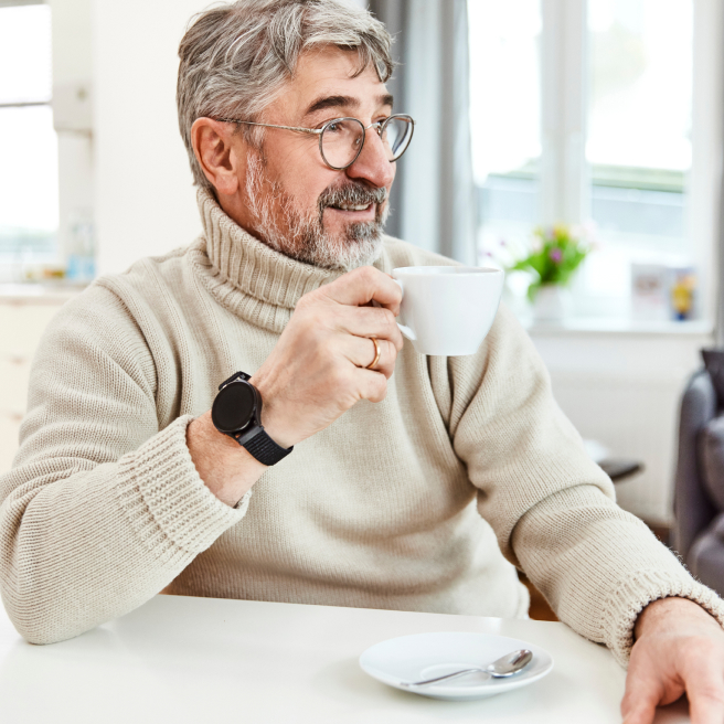 Mann mit Notfall-Armbanduhr bei Tasse Kaffee