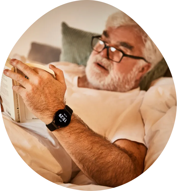 Senior mit Notfall-Uhr von Patronus liest ein Buch im Bett