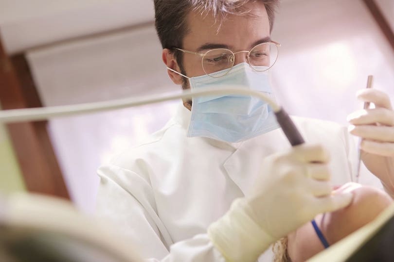 Zahnarzt mit Brille bei professioneller Zahnreinigung als Bonusprogramm der Krankenkasse