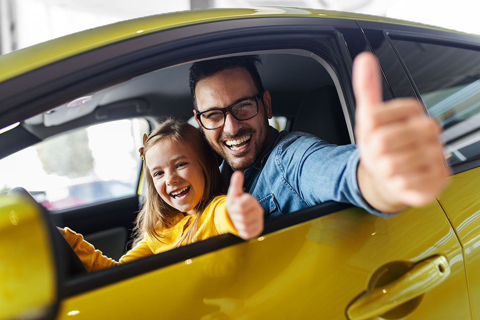 A father and daughter excitedly giving thumbs up while sitting in their new car