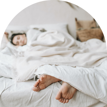 A woman sleeps in a bed with her toes sticking out from her white sheets.