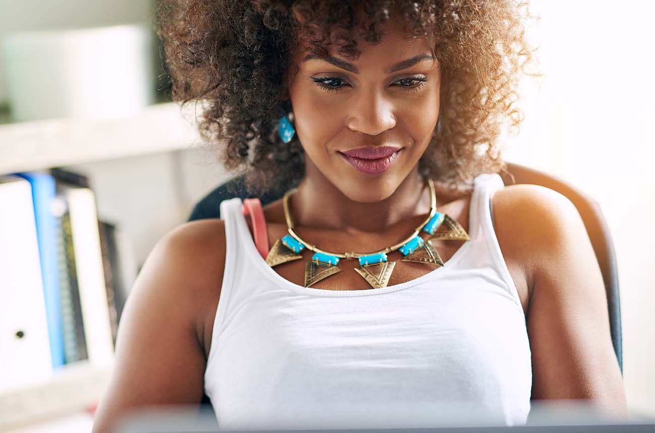 African American woman slightly smiling while looking at a laptop computer