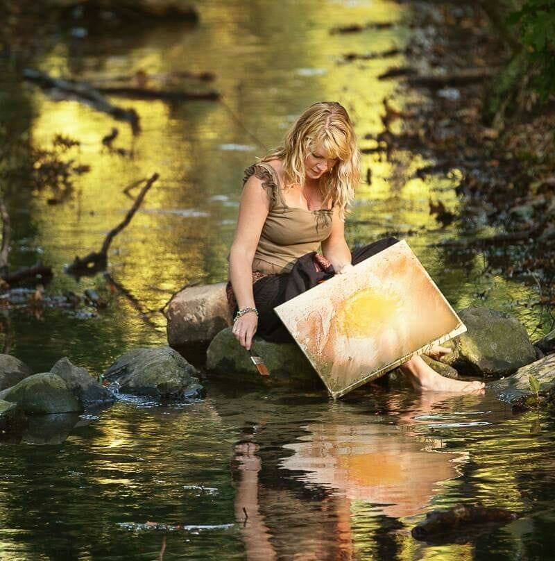 Suzan painting on rocks in the water.