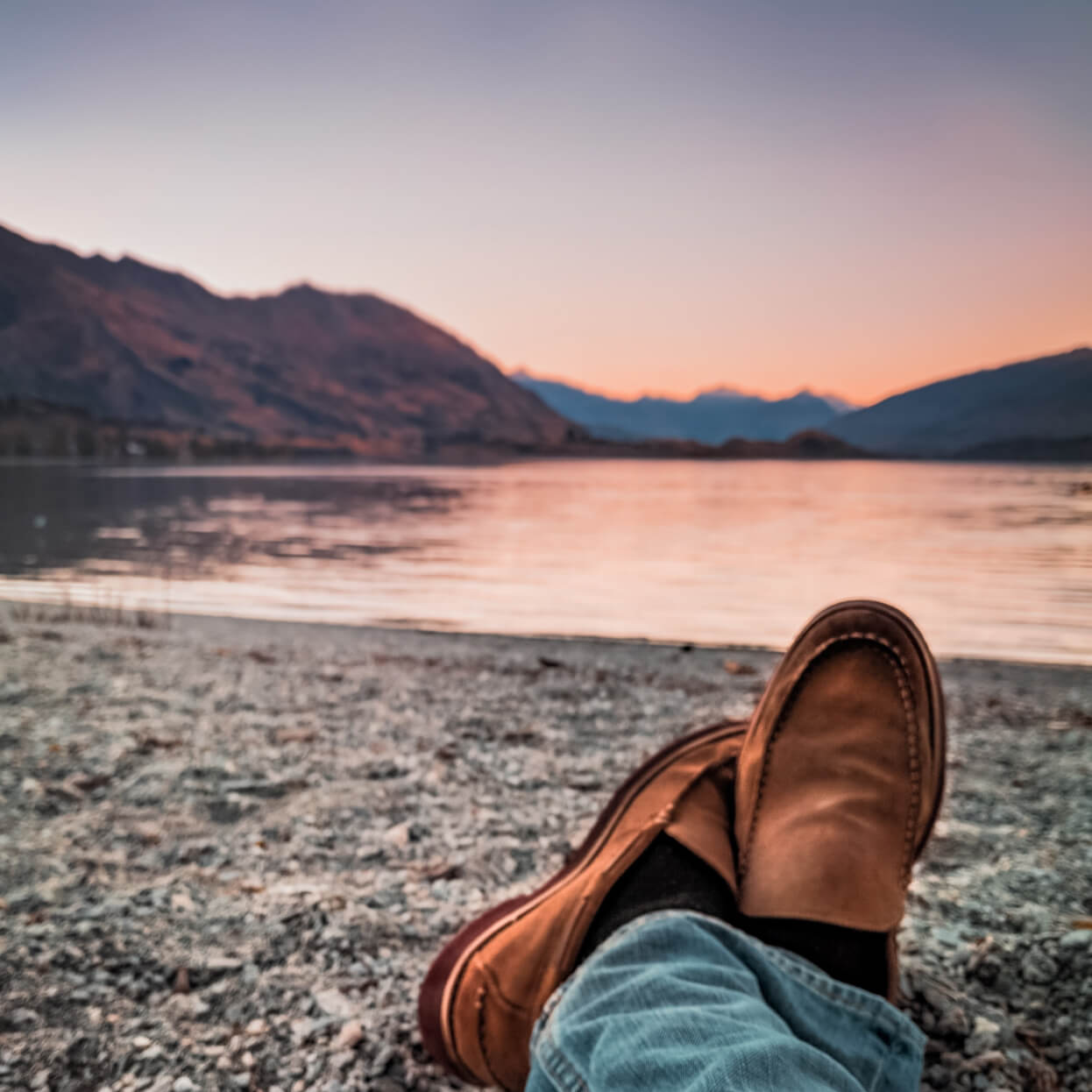 Someone laying on shore next to lake enjoying the sunset