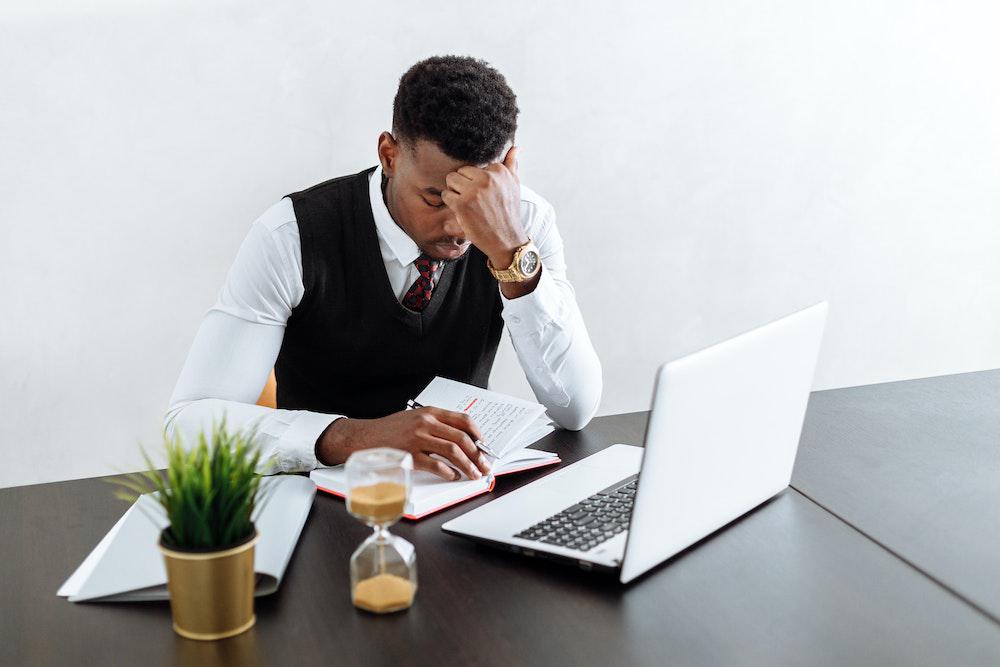 Man at table with laptop and notepad thinking