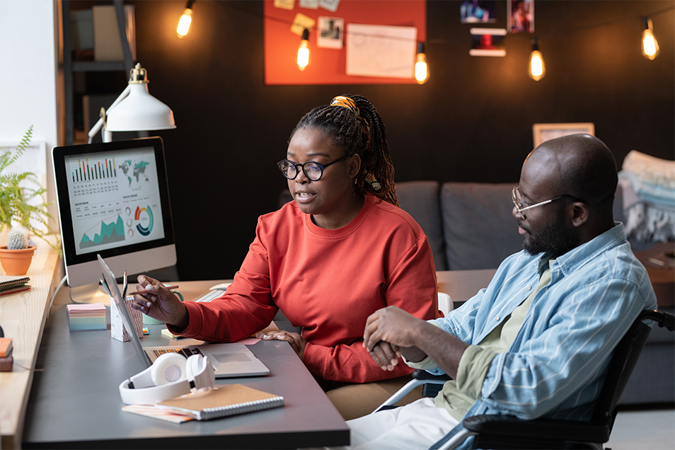 A woman and man discuss information on a MacBook Pro screen in front of them.