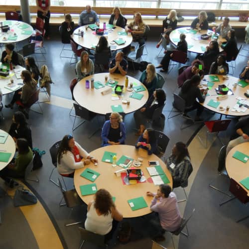 A large room with circular tables filled with people attending a conference.