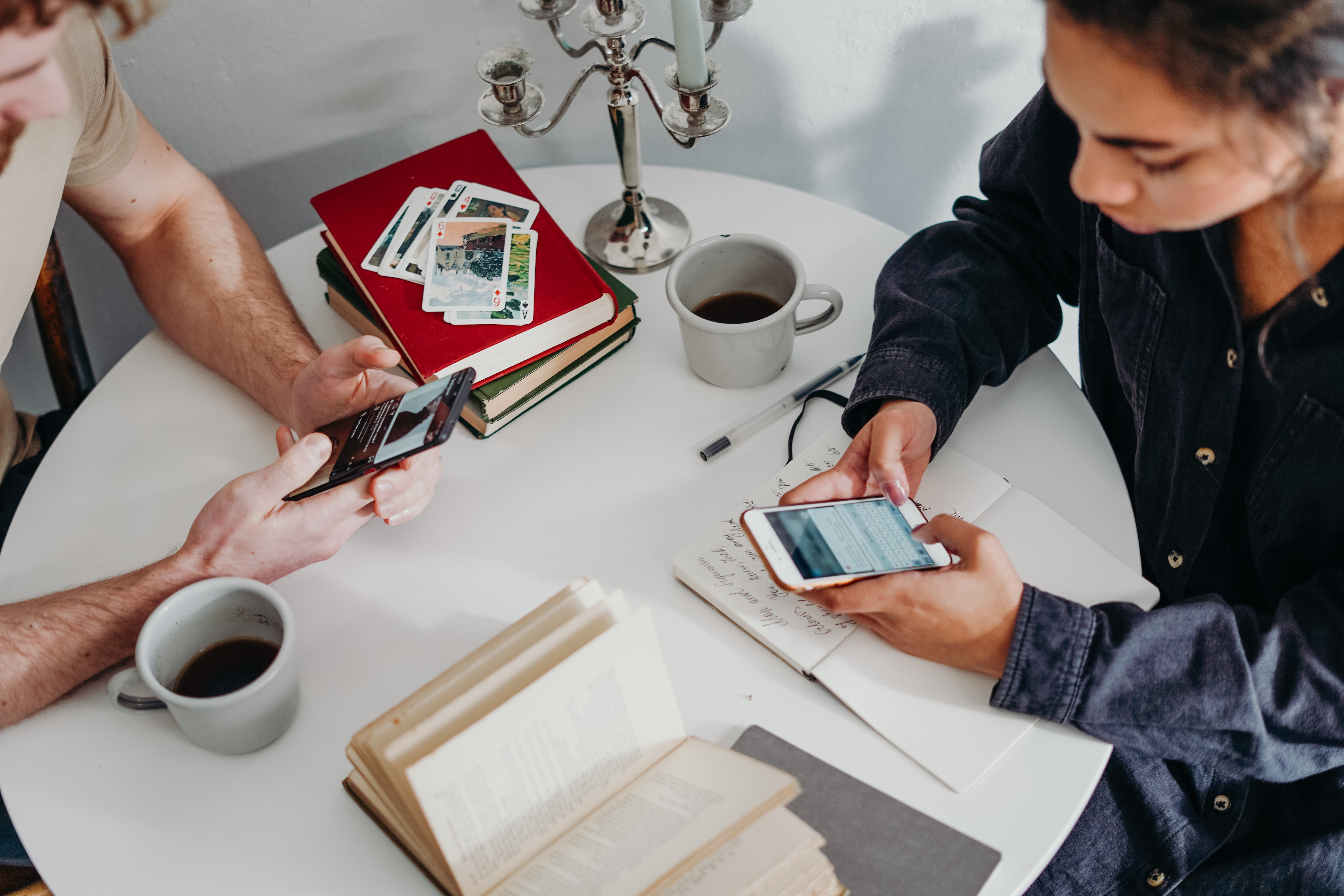 2 people sit at a table typing on smartphones