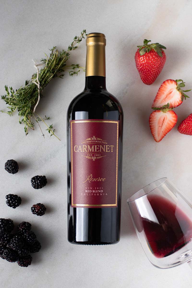 Carmenet Cabernet Sauvignon on marble with fresh fruit and a tipped-over wine glass